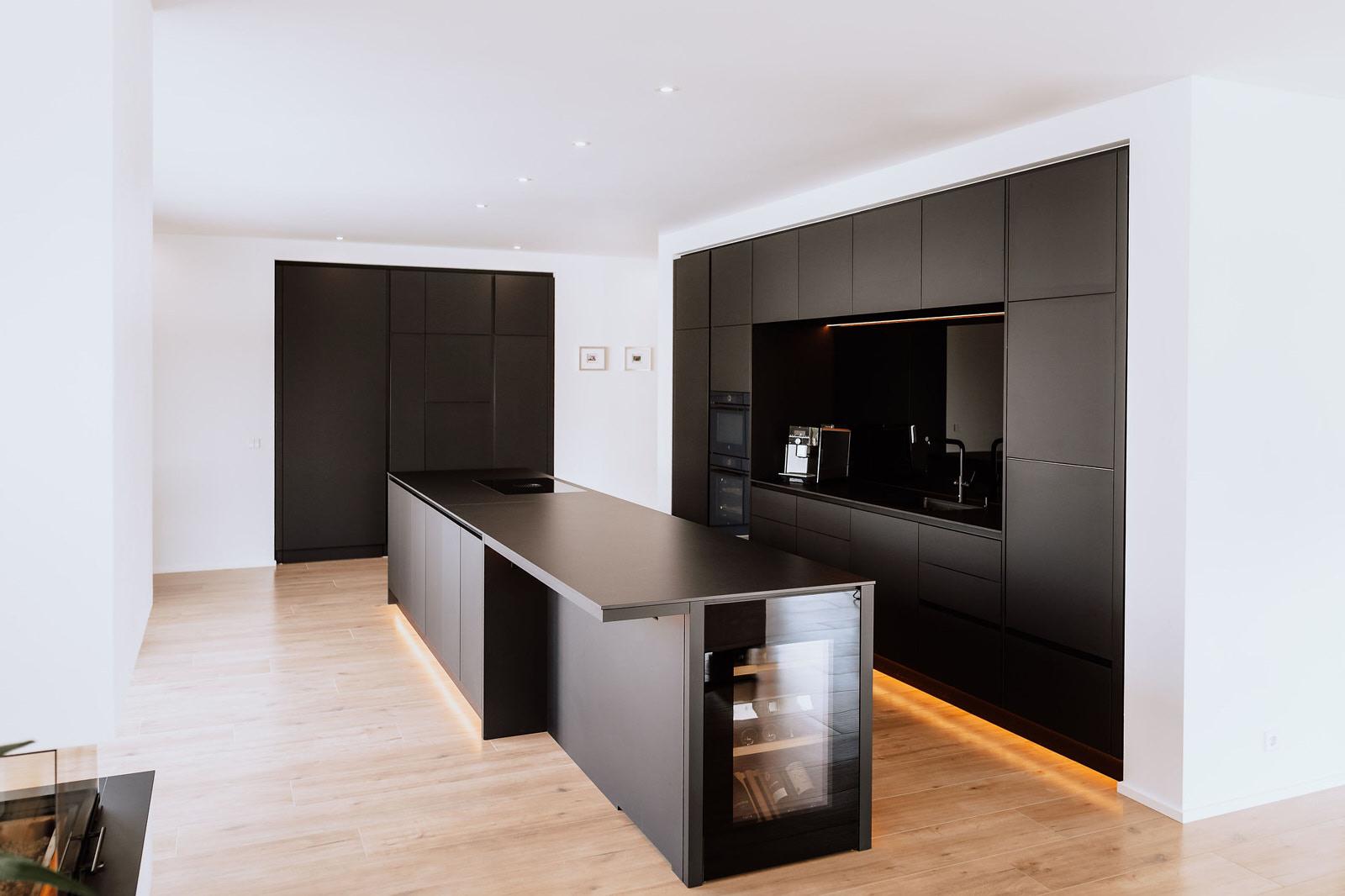 kuechenstudio-architektur-kueche-schwarz-haagschreinerei-bretten Offen gestaltete Hausbar / Partyküche mit erhöhter Theke und stimmungsvoll beleuchtetem Regalsystem als zentrales Element des Raums.